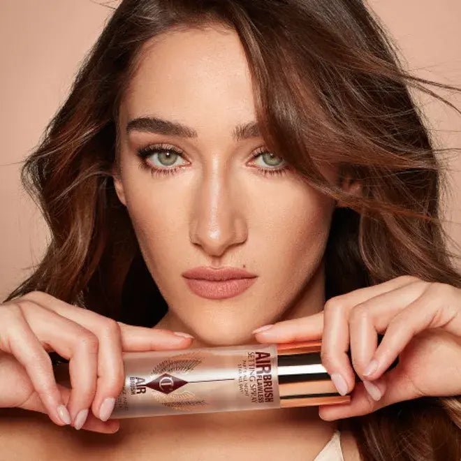 Woman holding Charlotte Tilbury Airbrush Flawless Setting Spray 100ml with a neutral background