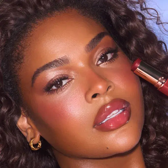 Close-up of a woman applying Cherry Glow Blush Stick of Charlotte Tilbury with a blue background
