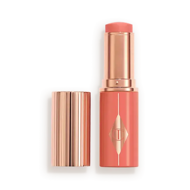 Peachy Glow Blush Stick of Charlotte Tilbury with a metallic rose gold tube, shown with the cap off next to the tube on a white background.