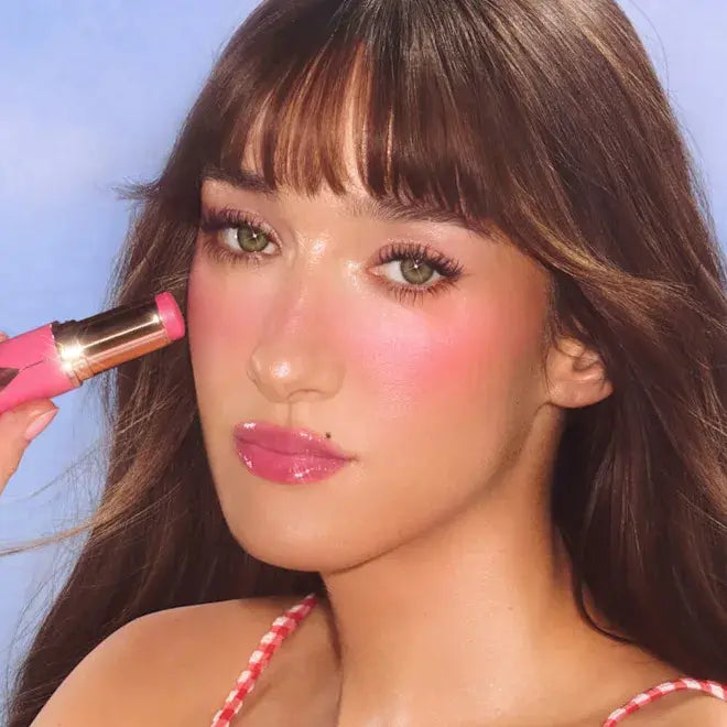Woman applying Pinky Glow Blush Stick of Charlotte Tilbury against a blue background