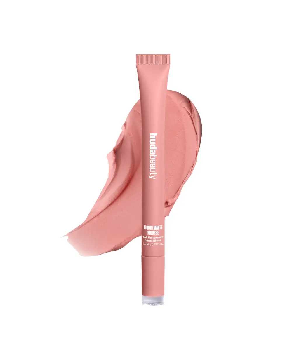 A tube of Huda Beauty Liquid Matte Mousse in a dusty rose pink shade, shown upright in front of a matching cream-colored product smear on a solid white background.