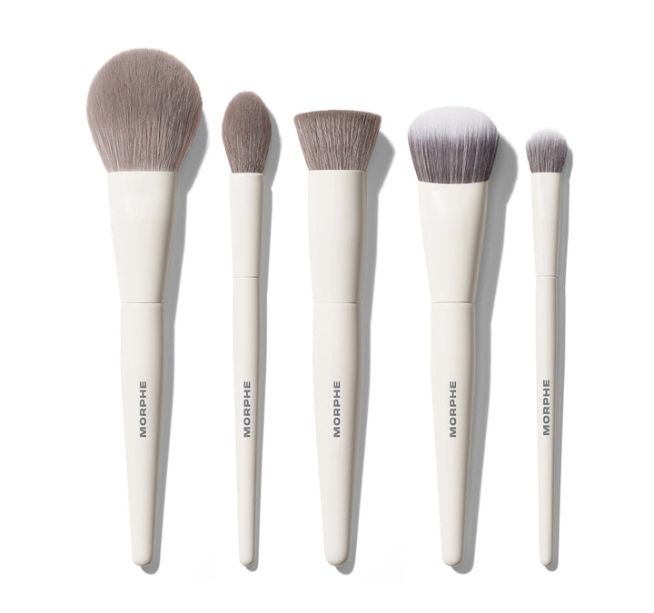 Six Morphe makeup brushes in different sizes, arranged in a row on a clean white background. The brushes feature soft, light brown bristles and sleek, matte white handles with the brand name 'MORPHE' printed vertically in gray.