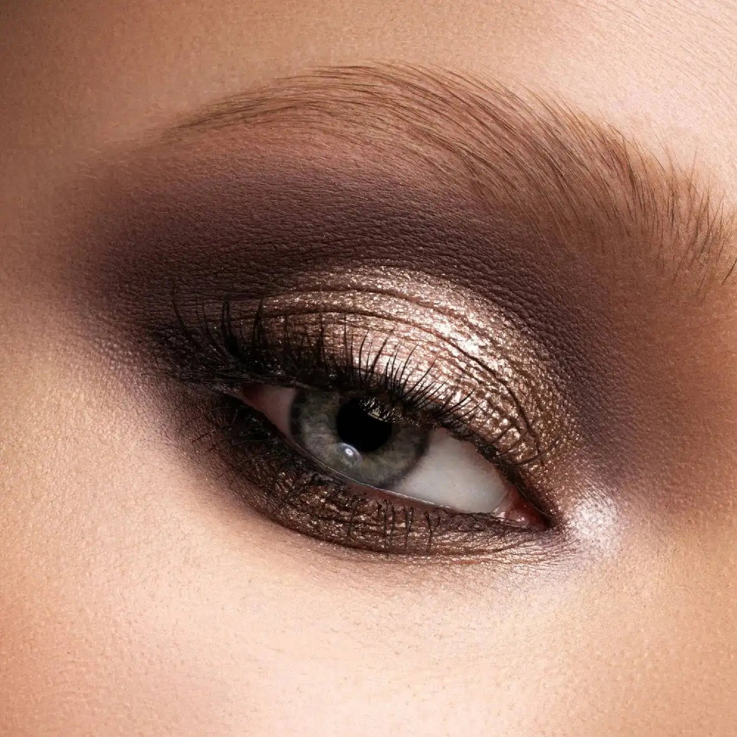 Close-up of a model eye wearing Natasha Denona I need a Nude Palette eyeshadow in bronze, brown, and gold tones with long lashes and a defined eyebrow.