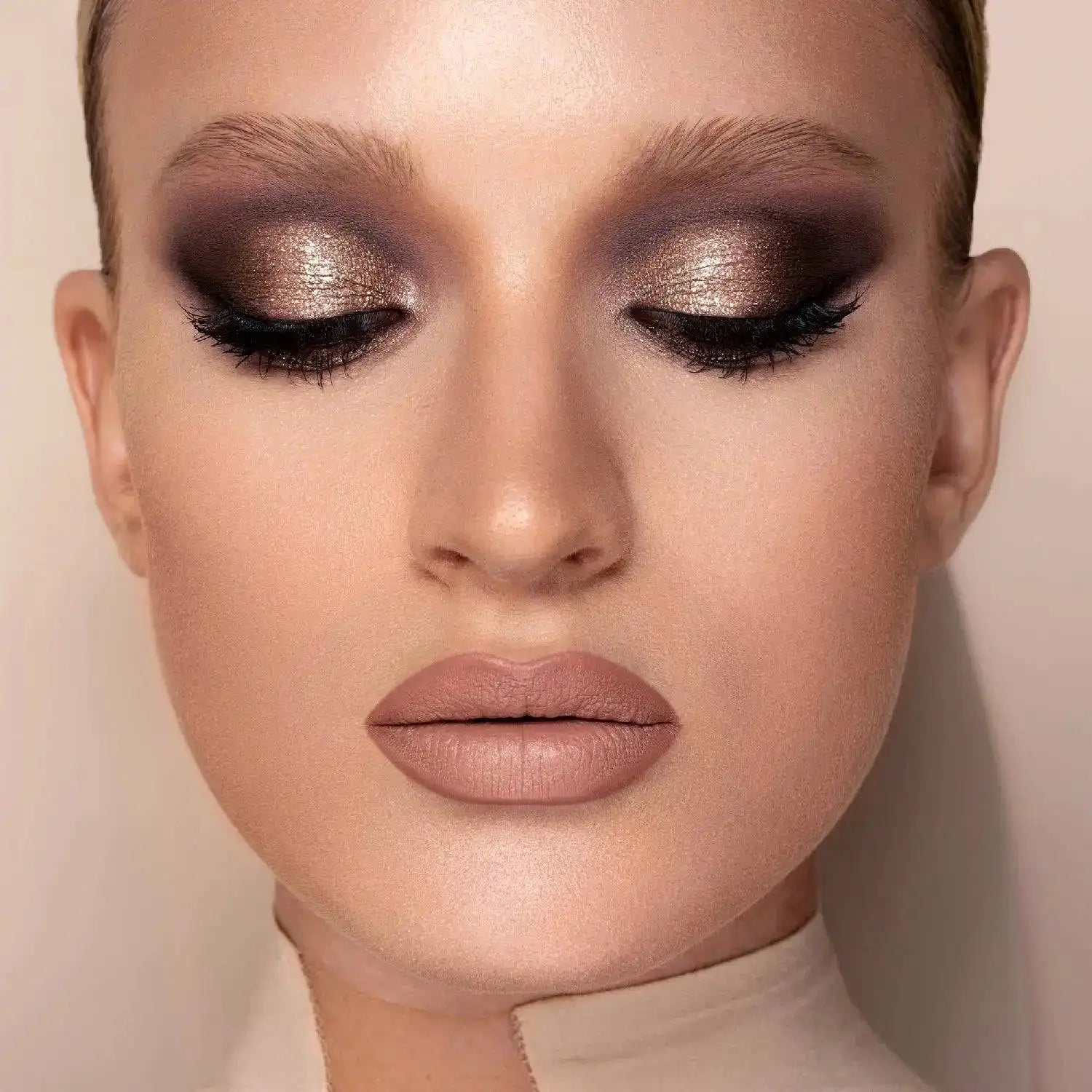 Close-up of a model with Natasha Denona I need a Nude Palette makeup featuring shimmery bronze and dark brown eyeshadow, black eyeliner, and nude pink lipstick.